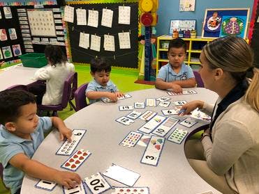 Adult and three children playing with number cards at a table in a classroom
