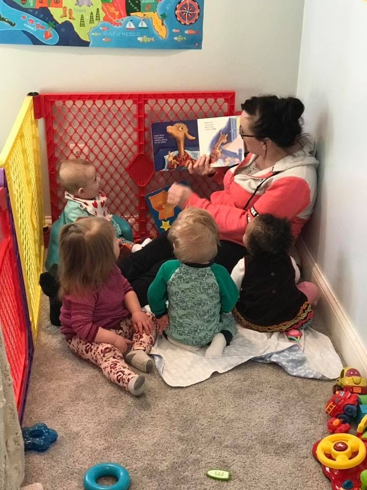 Person reading a book to four children in a playpen