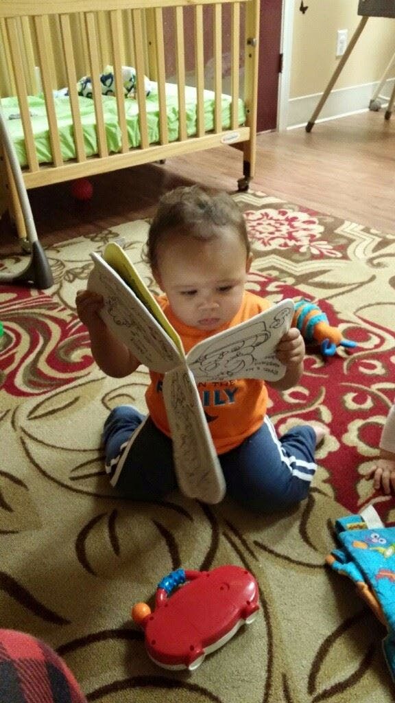 Child kneeling on a rug, holding an open book