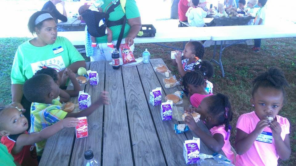 Adults and children eating at a picnic table outdoors