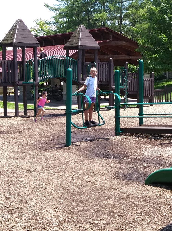 Child on playground equipment, another child running in background