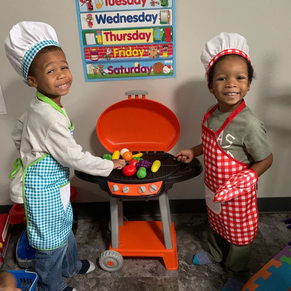 Two children playing with a toy grill and toy food