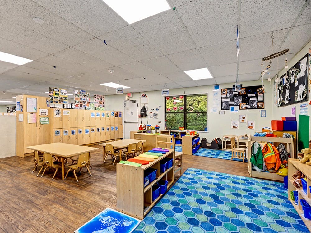 Classroom with small tables and chairs, storage cubbies, and a blue rug
