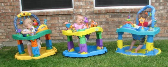 Three children in colorful activity centers on grass