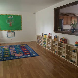 Classroom with a colorful rug, green bulletin board, and shelves with toys