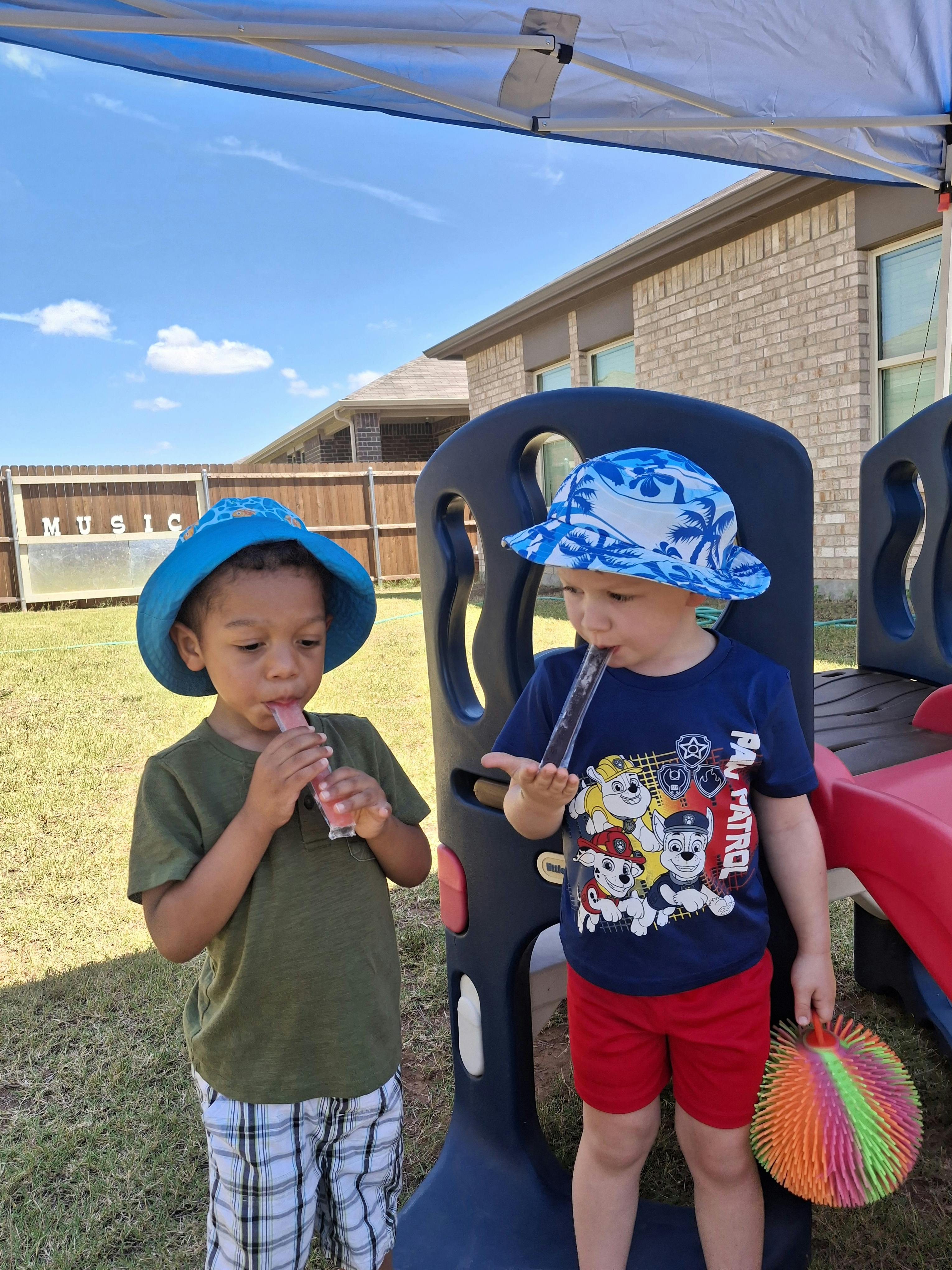 Two children in hats eating popsicles outdoors