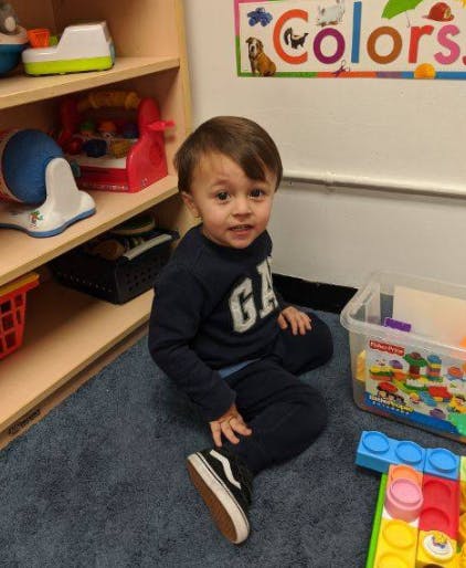 Child sitting on a rug next to shelves with toys