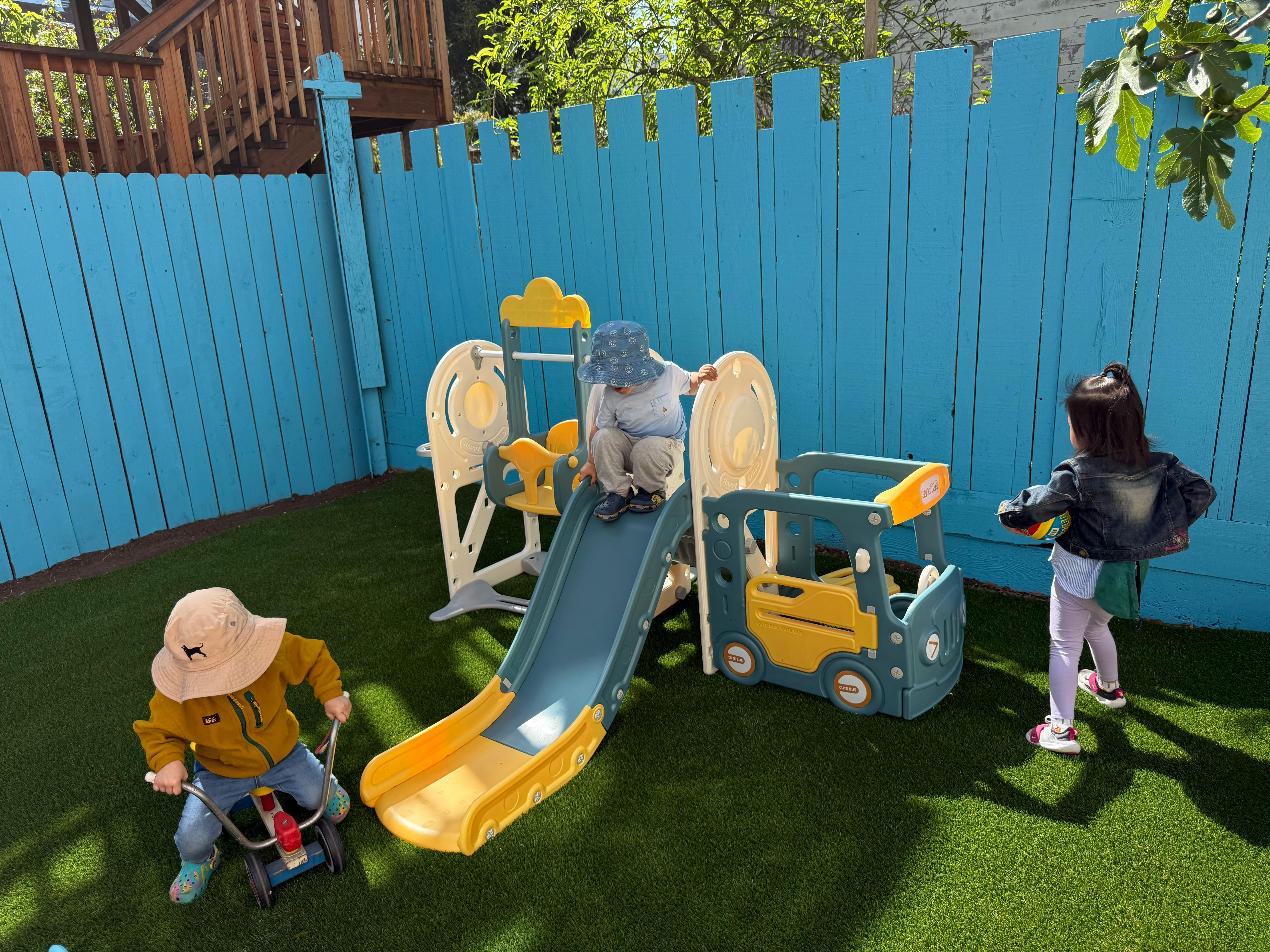 Two children playing on a slide and ride-on toy in a backyard