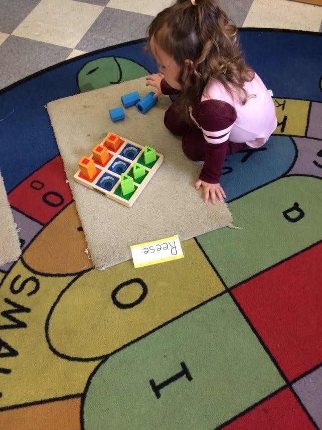 Child playing with a colorful shape sorting toy on a rug
