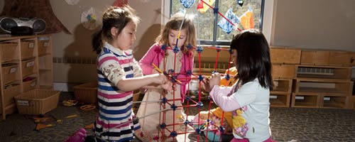 Three children building with a construction toy in a classroom
