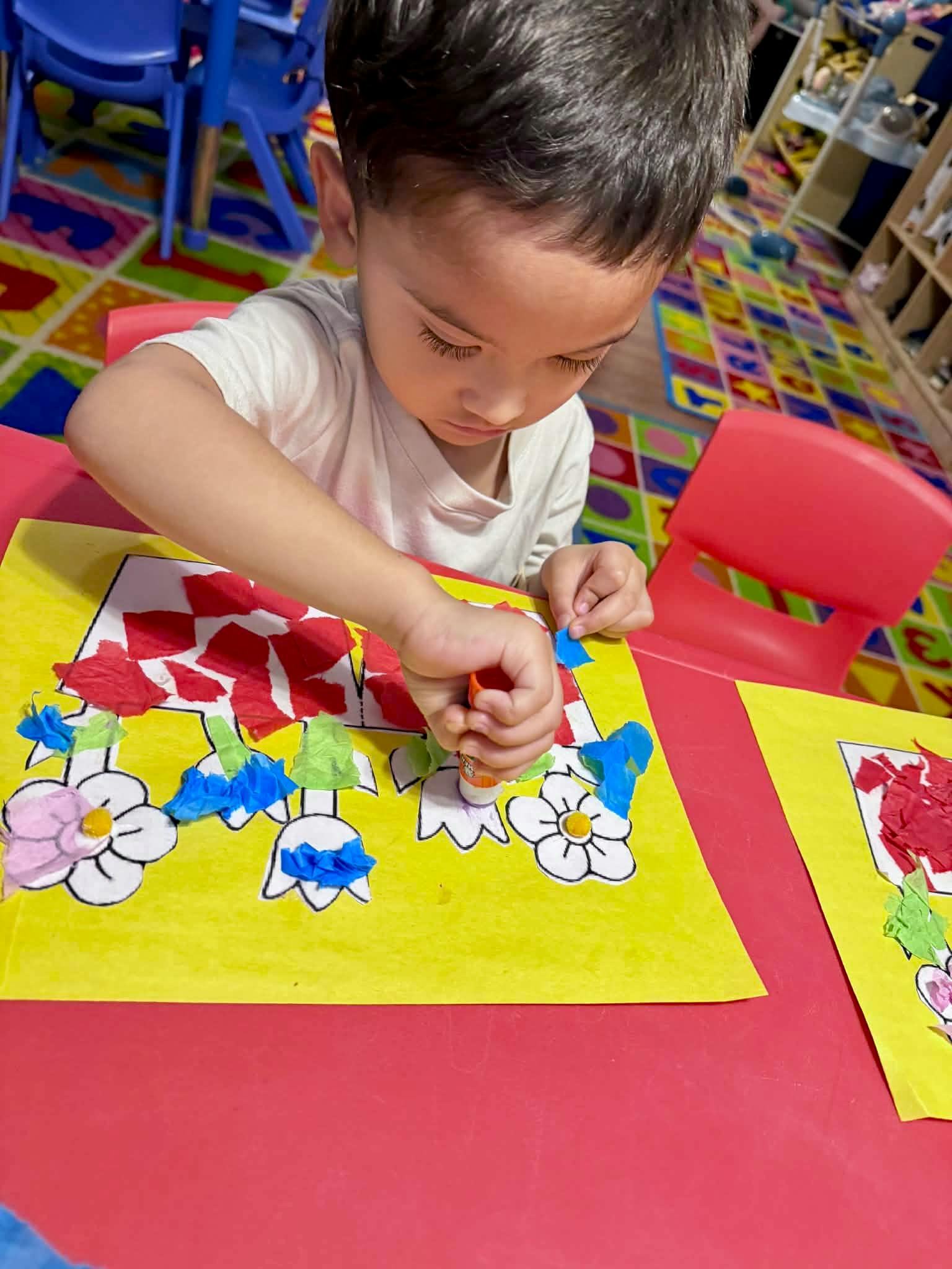 Child gluing pieces of paper onto a flower-themed craft at a table