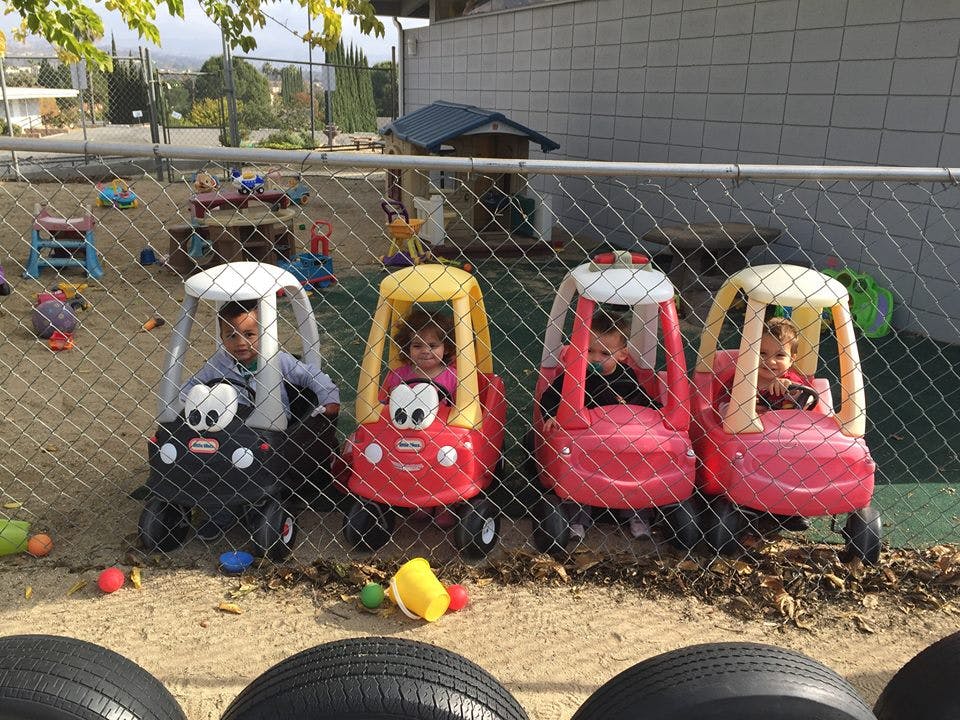 Children playing in toy cars behind a fence