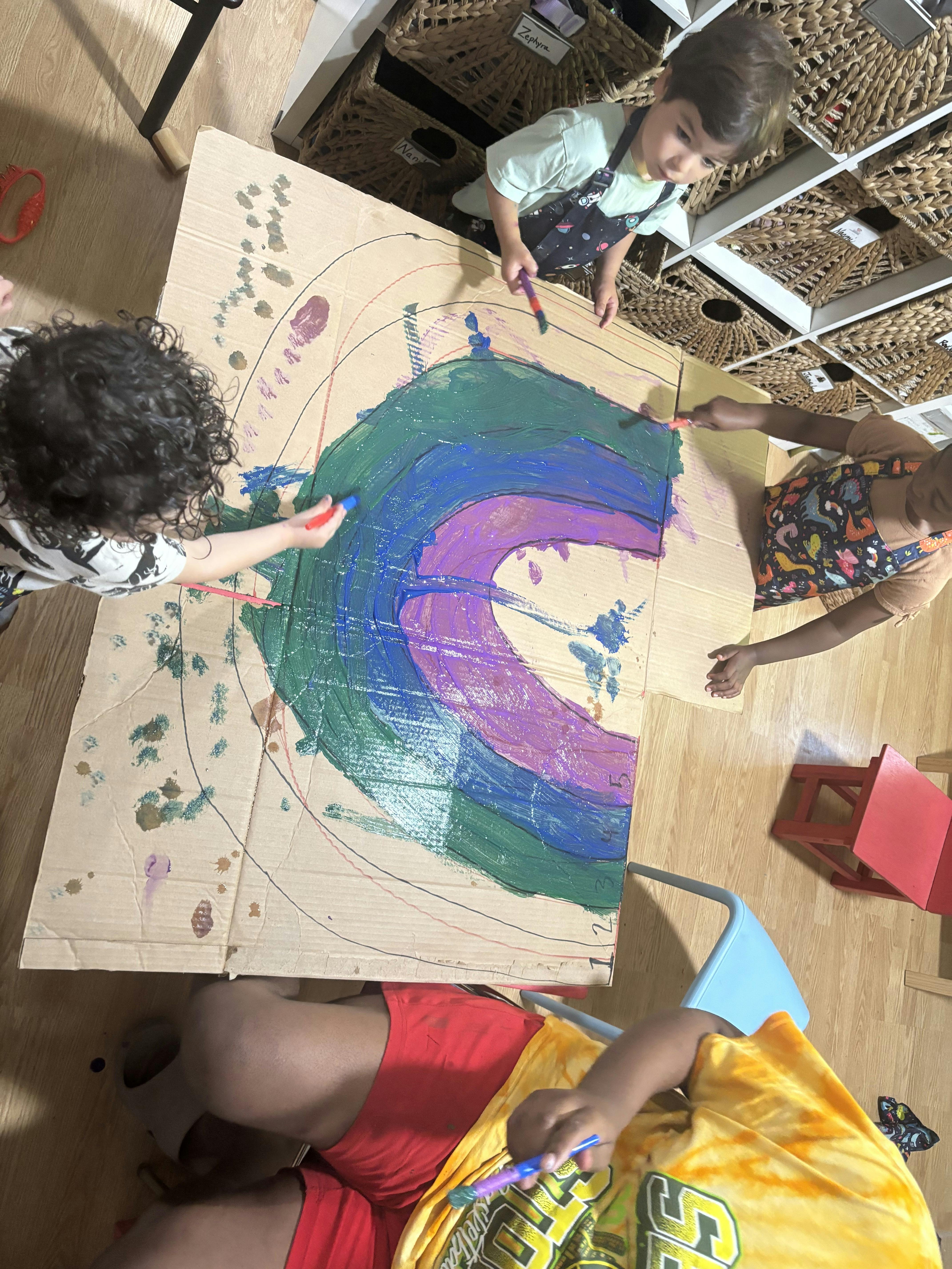 People painting a large rainbow on cardboard