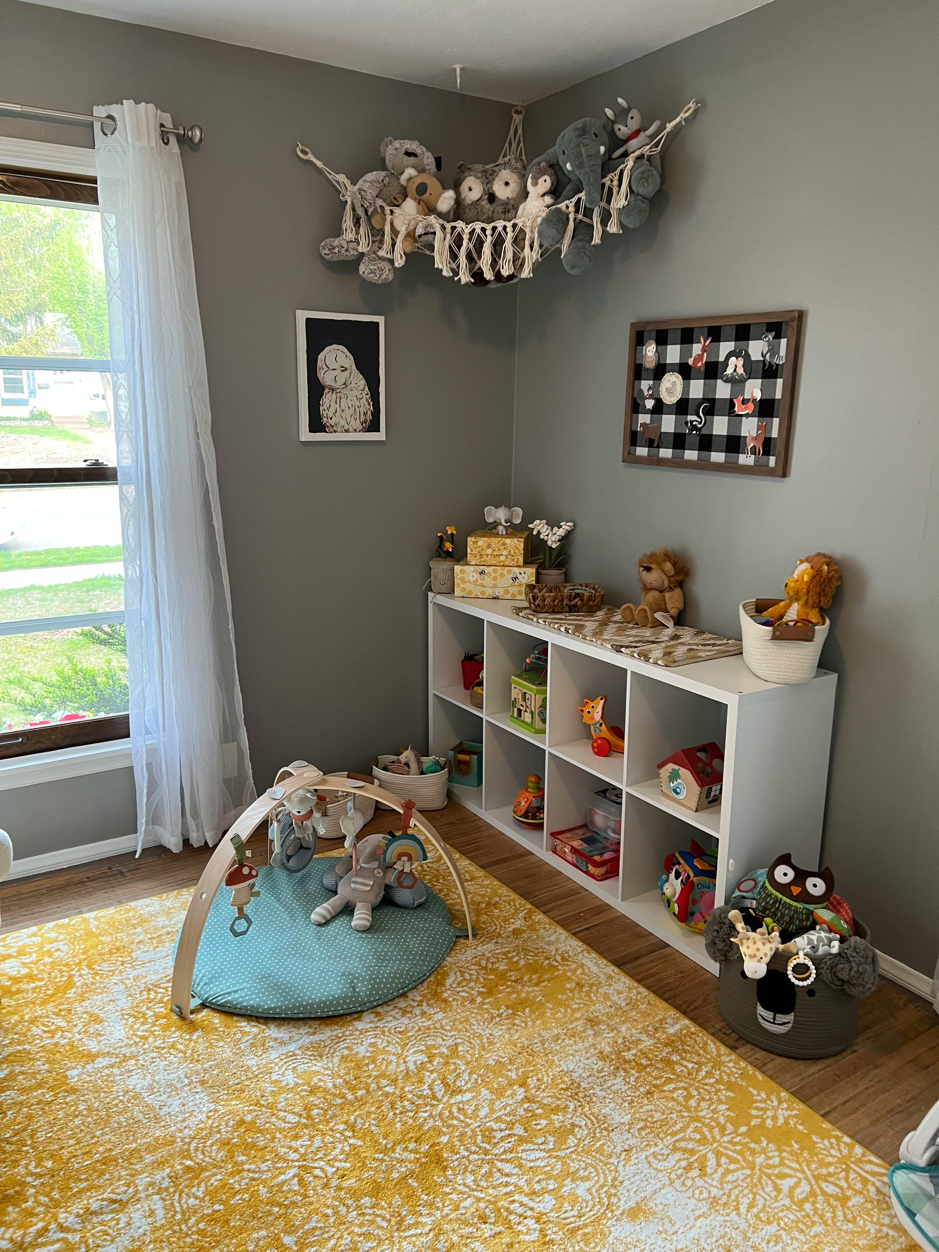 Nursery room with a play mat, toy shelf, and stuffed animals in a hanging net