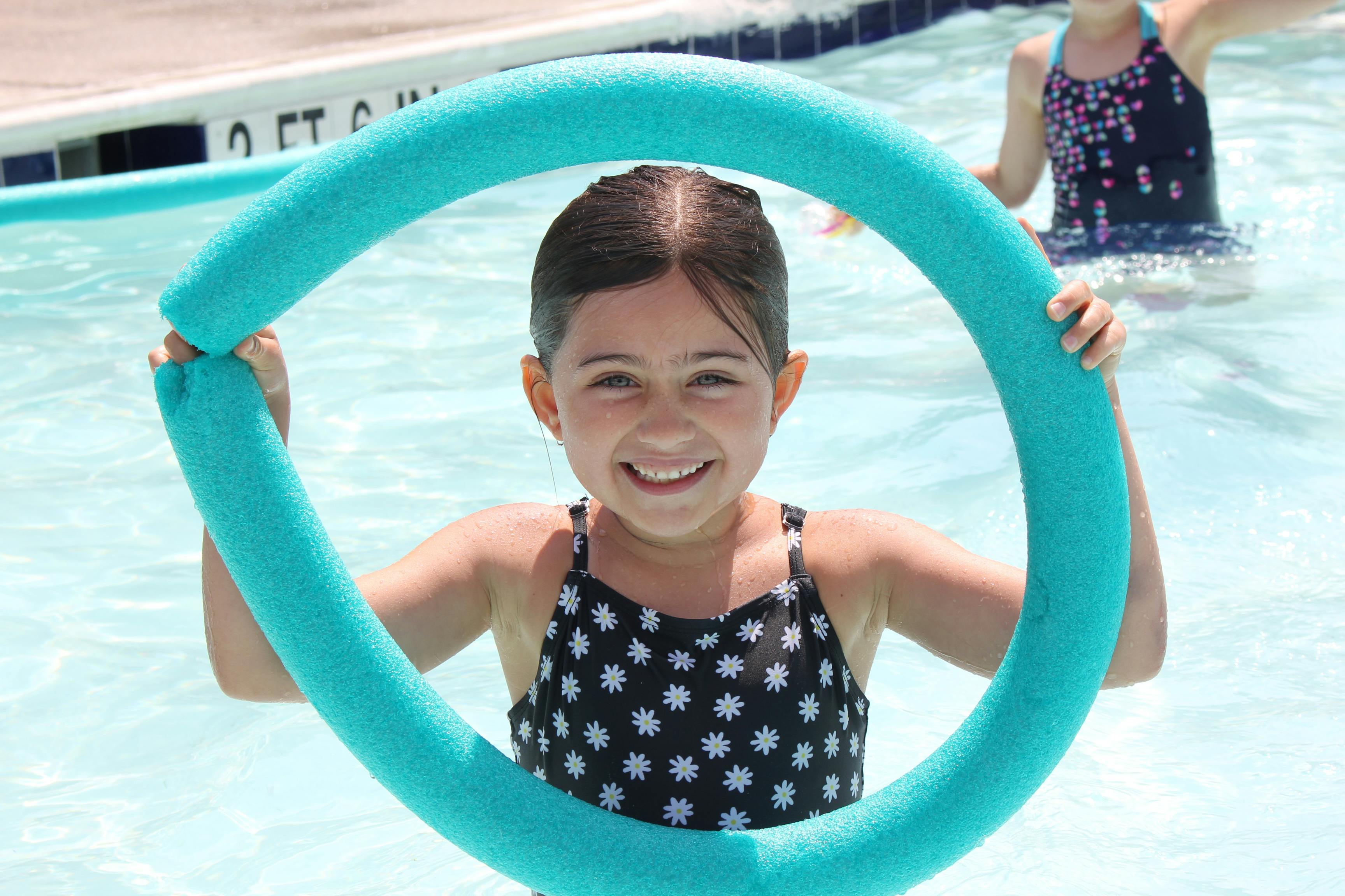 Child in a swimming pool holding a blue pool noodle
