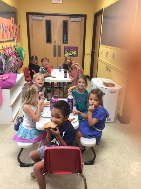Children eating pizza at tables in a classroom