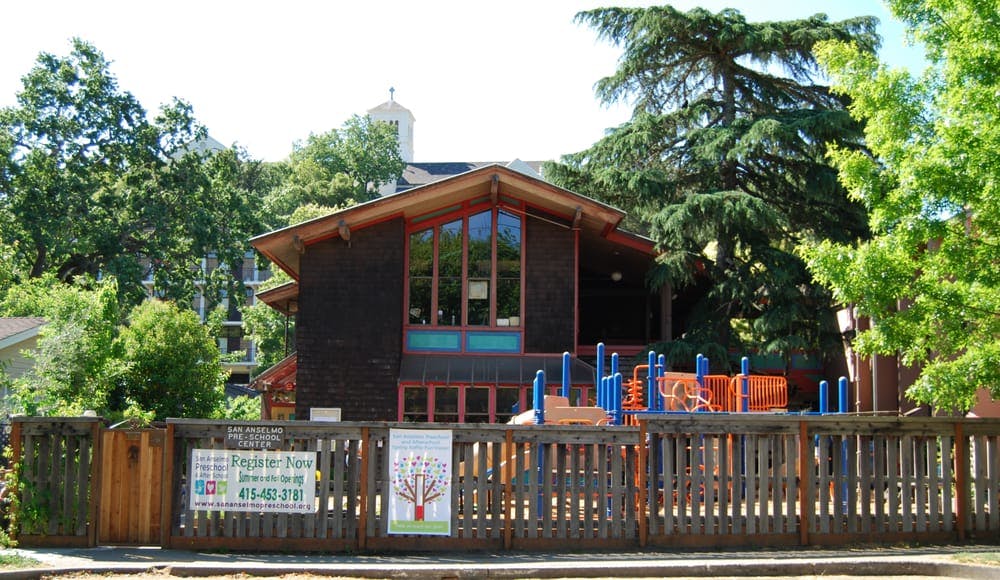 Building with large windows behind a wooden fence and playground equipment