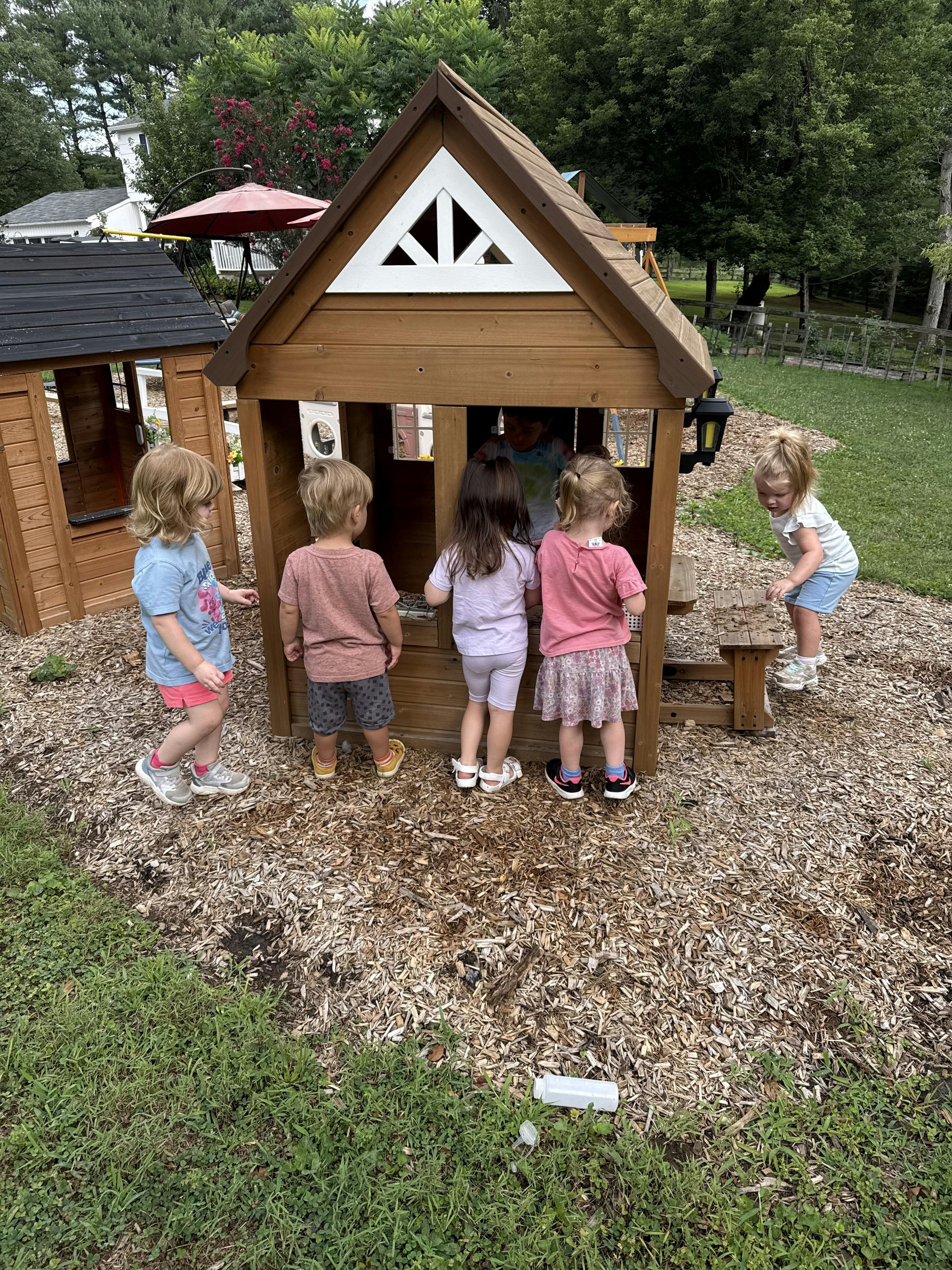 Group of children playing around a wooden playhouse in an outdoor area