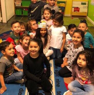 Group of children gathered on a rug, one child wearing a crown