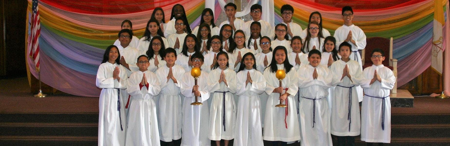 Group of children and teens in white robes, some holding candles or with hands together