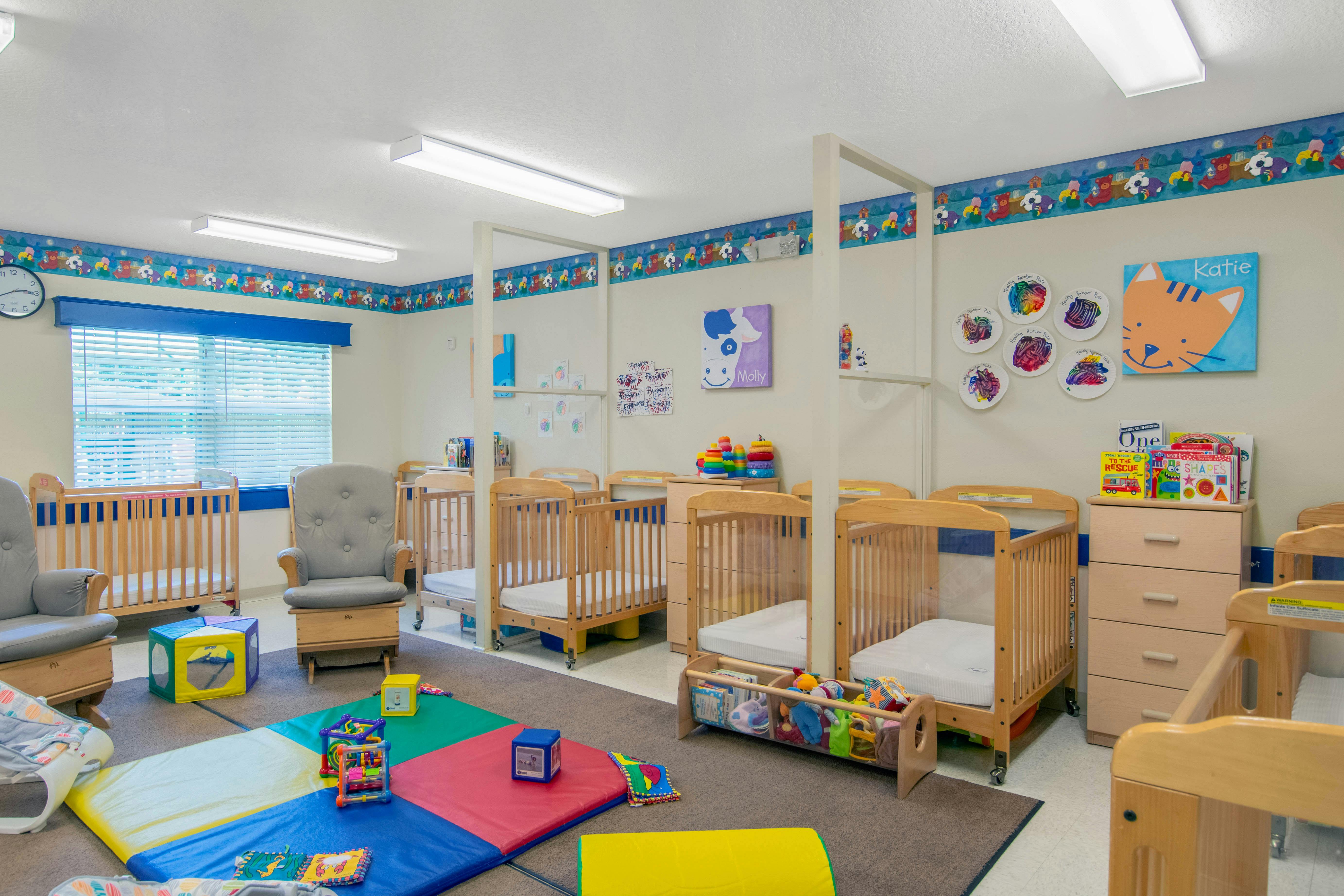 A colorful childcare classroom with several cribs, rocking chairs, and toys