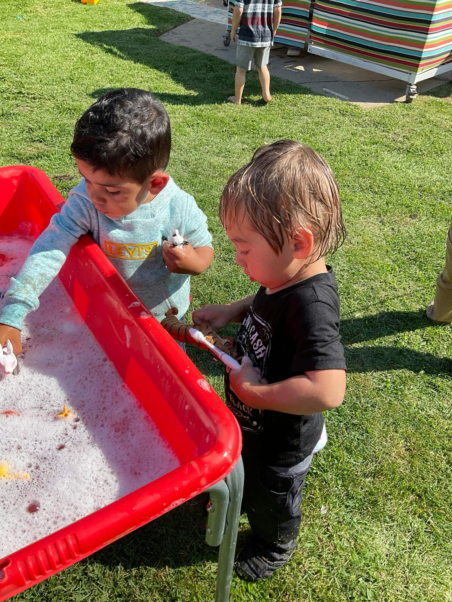 Two children playing with toys in a red tub filled with soapy water