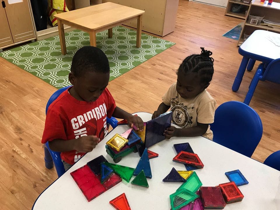 Two children playing with colorful magnetic shapes at a table