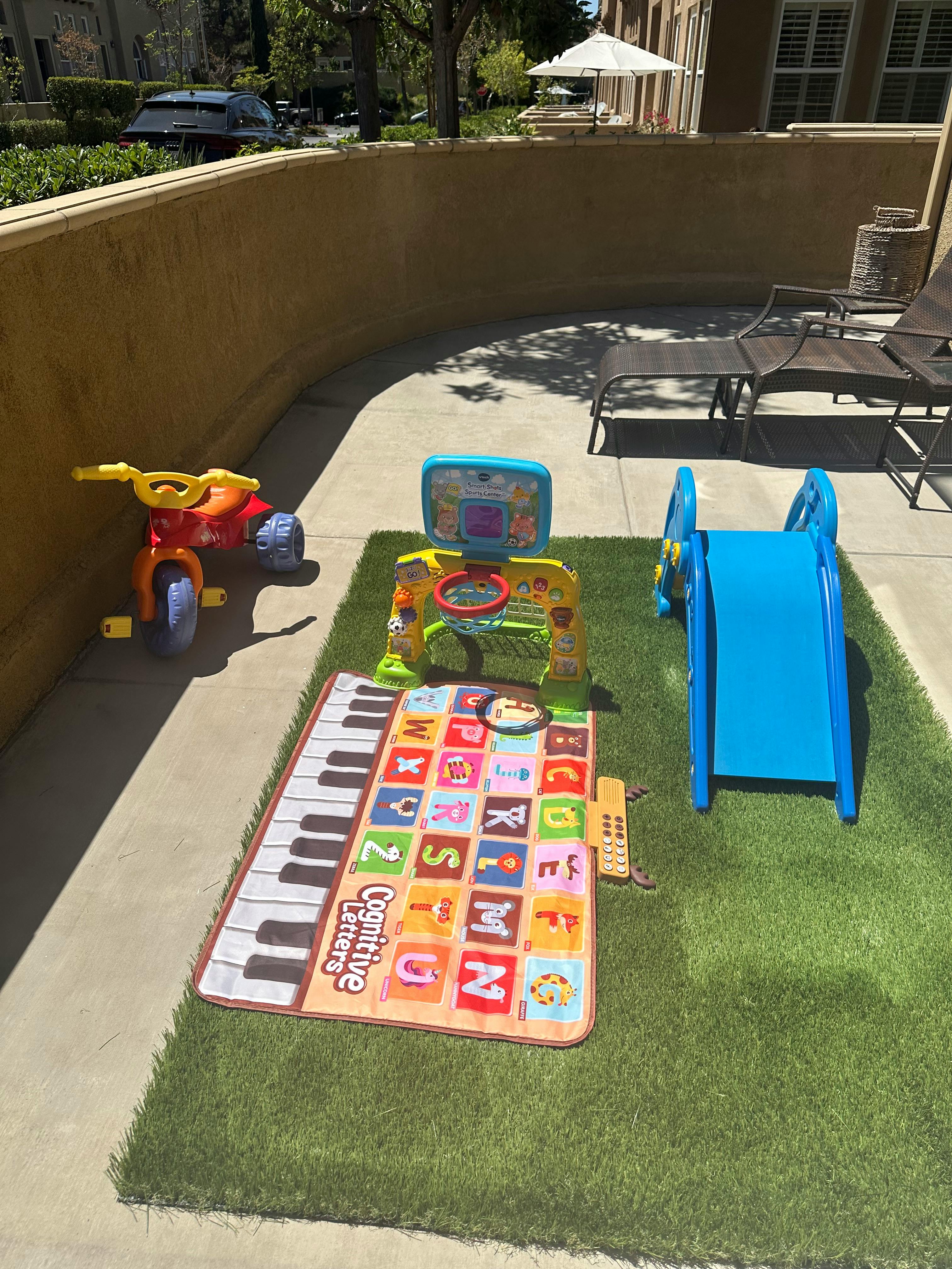 Children's toys including a tricycle, slide, and playmat on artificial grass