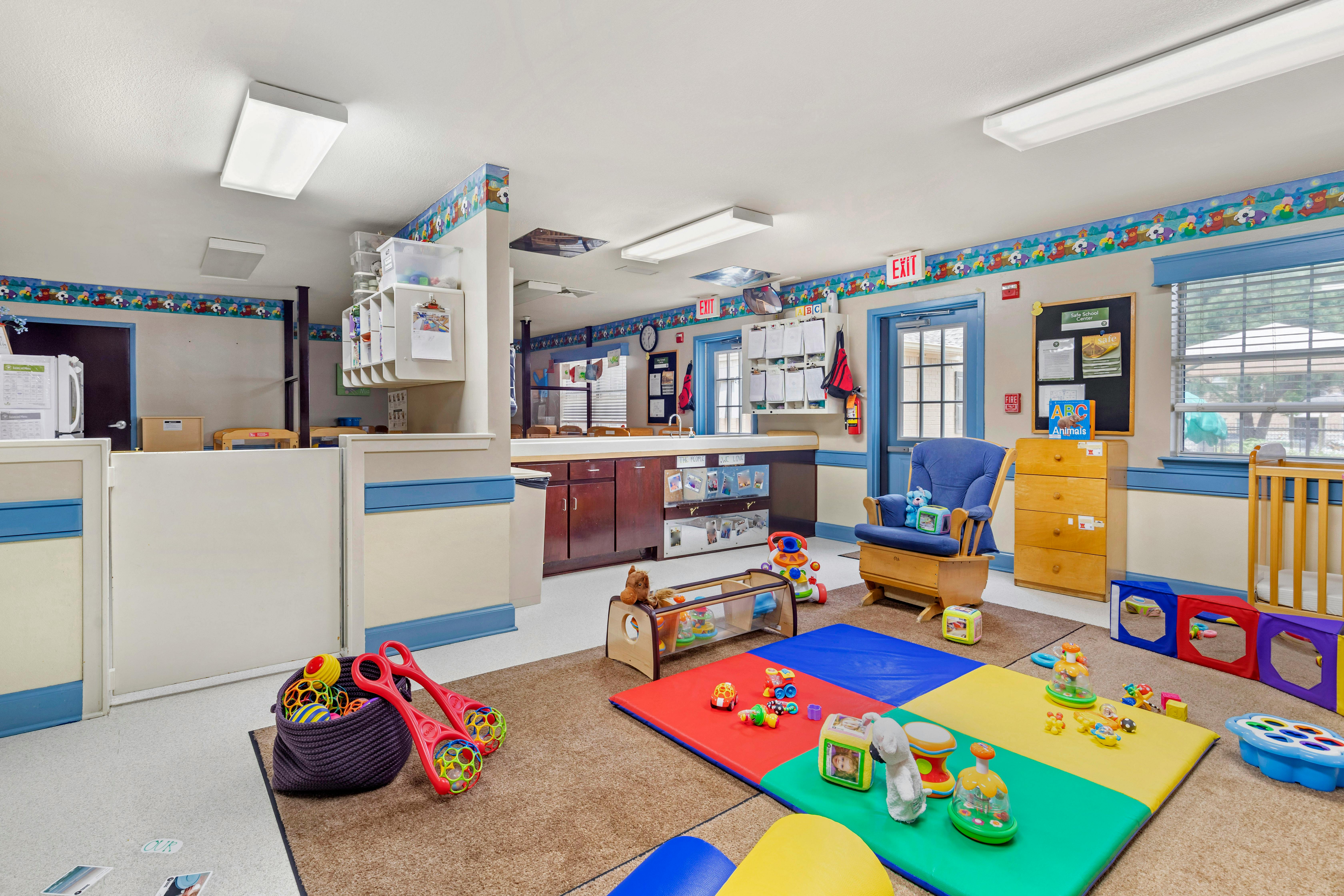 An empty infant classroom with colorful mats and various baby toys on the floor