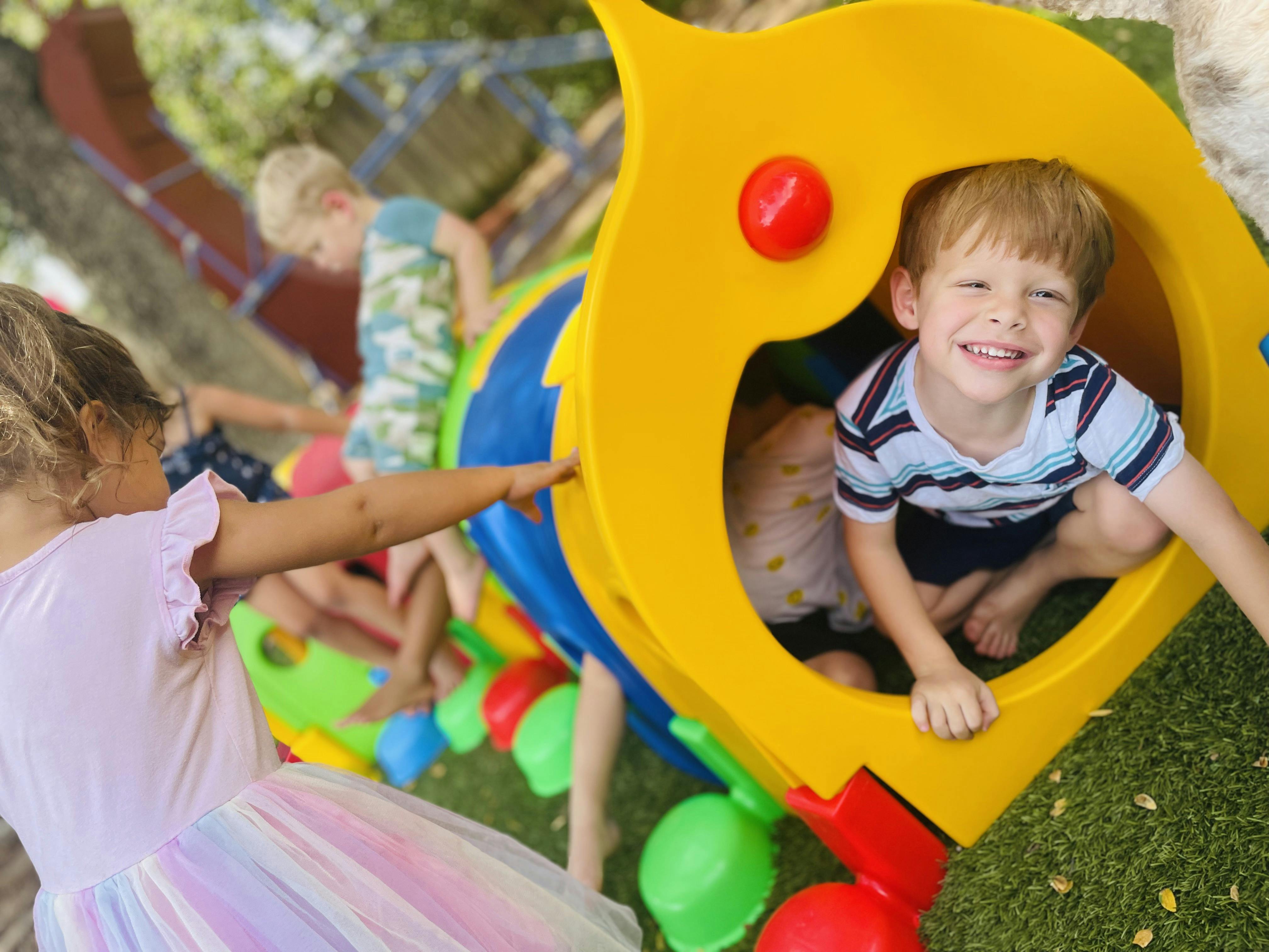 Child in a yellow play structure with other children playing nearby