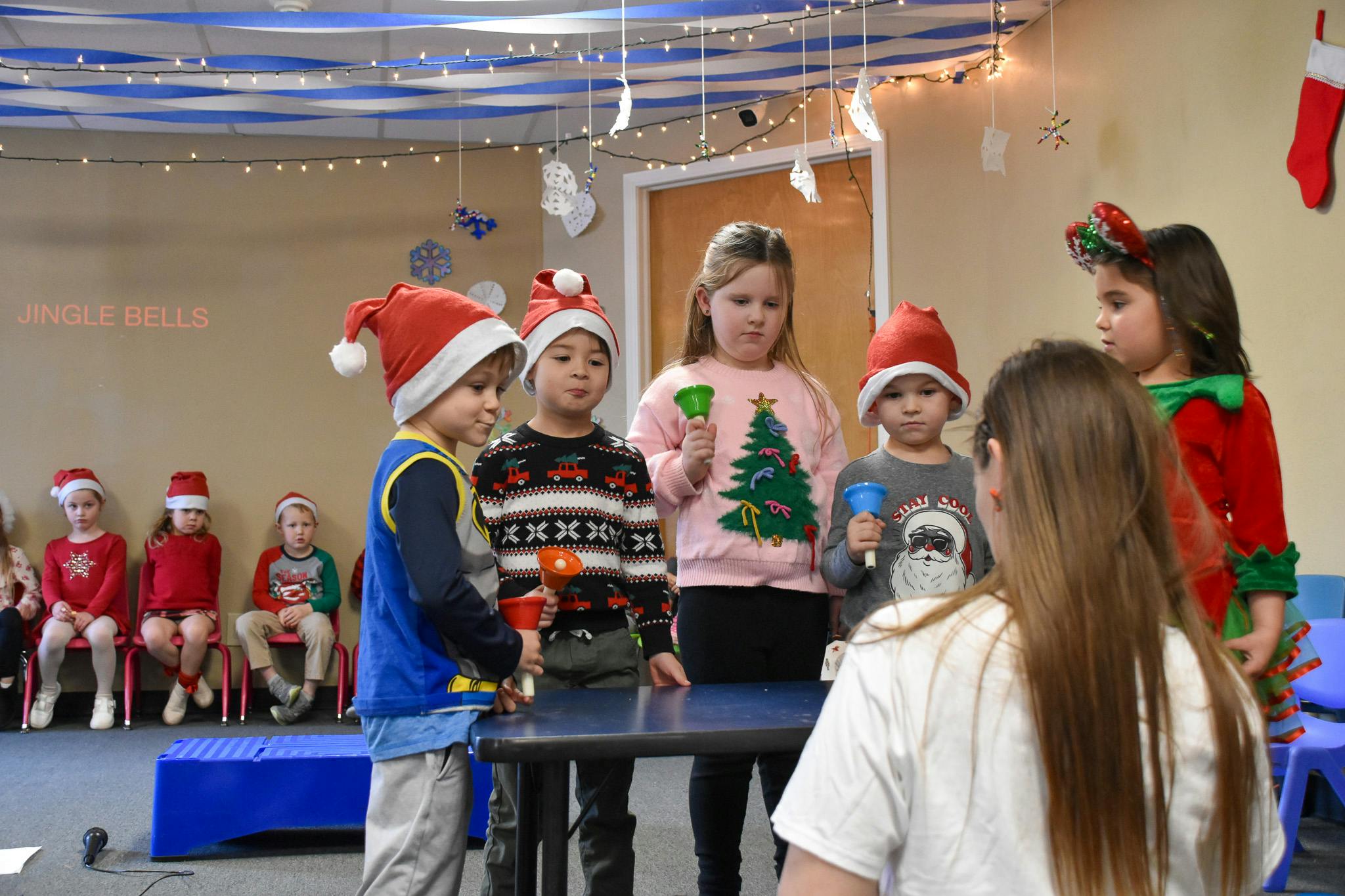 Children in holiday attire holding handbells, text "JINGLE BELLS" on wall