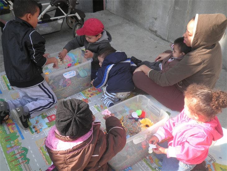Adult and children playing with toys in clear bins on a mat