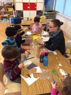 Adult and children doing crafts at a table in a classroom