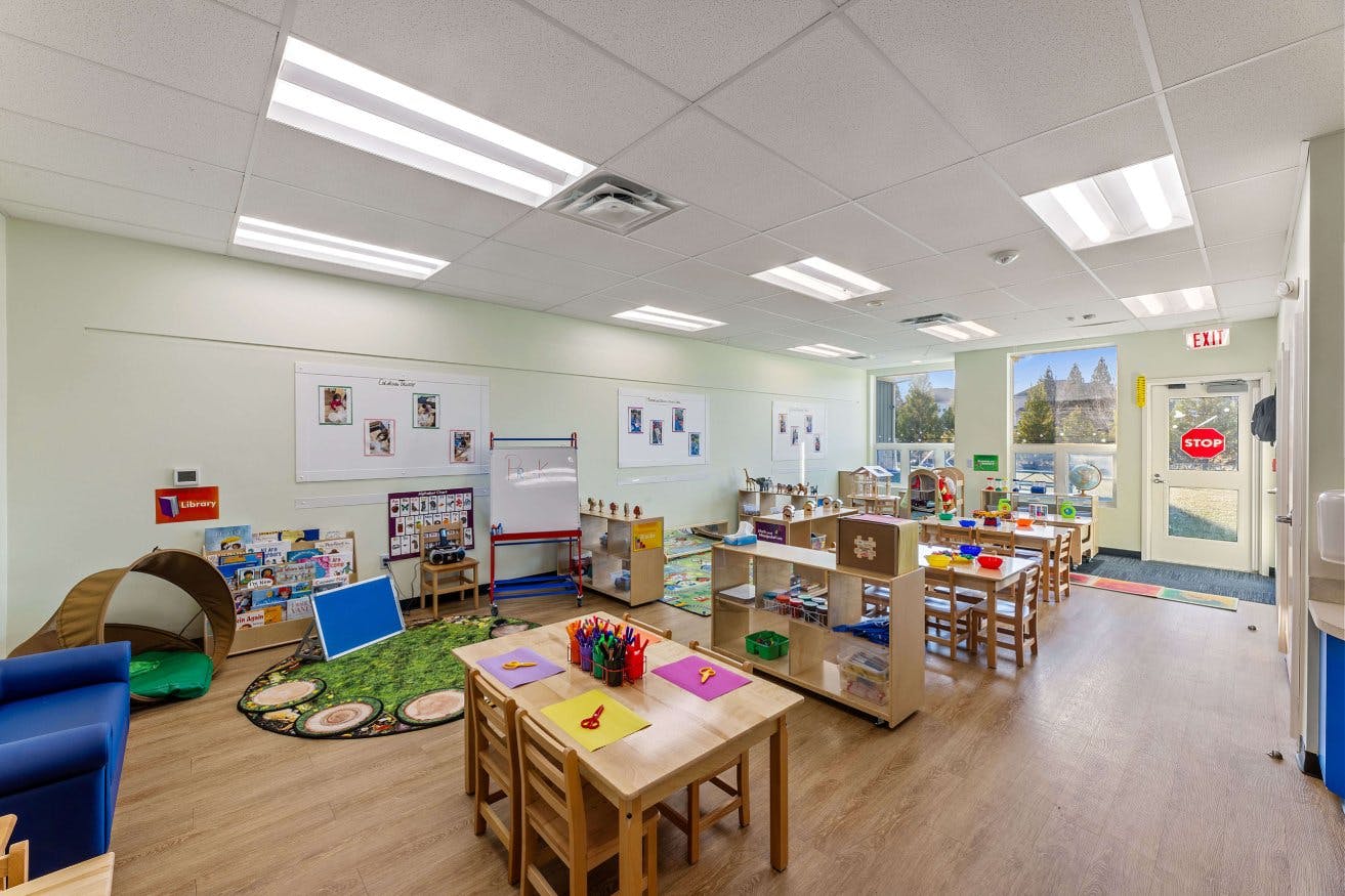Empty classroom with small tables and chairs, shelves, and a reading nook