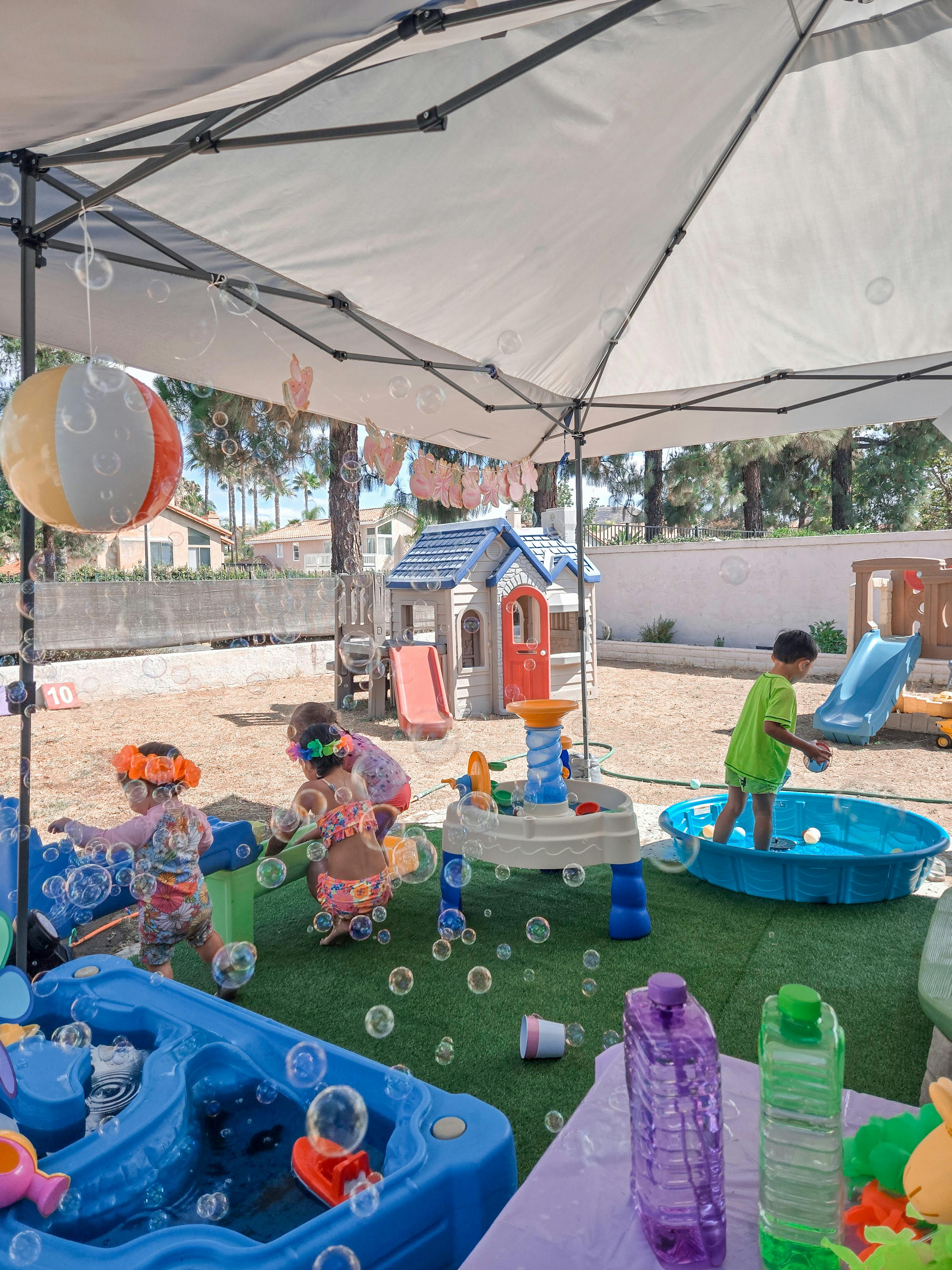 Children playing with water tables and a pool under a canopy tent