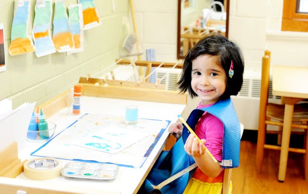 Child painting at a desk in a classroom