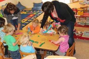 Two adults and multiple children playing with colorful objects at a table