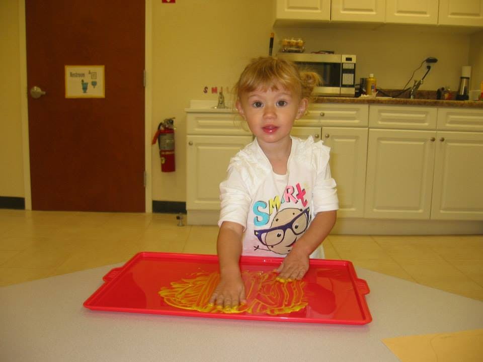 Child playing with yellow material on a red tray