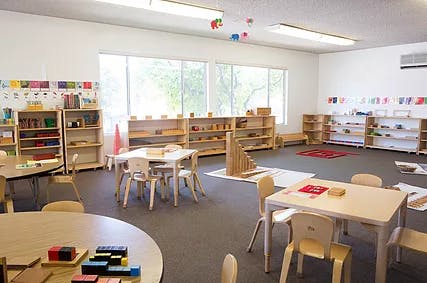 Empty classroom with small tables, chairs, and shelves with learning materials