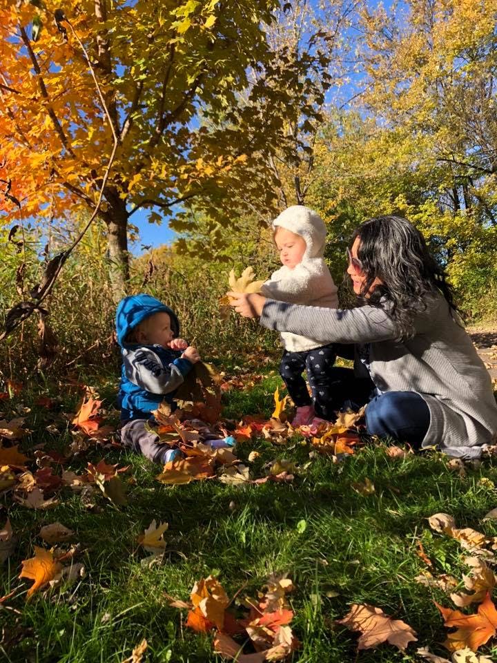 Person and two children playing with autumn leaves on the grass