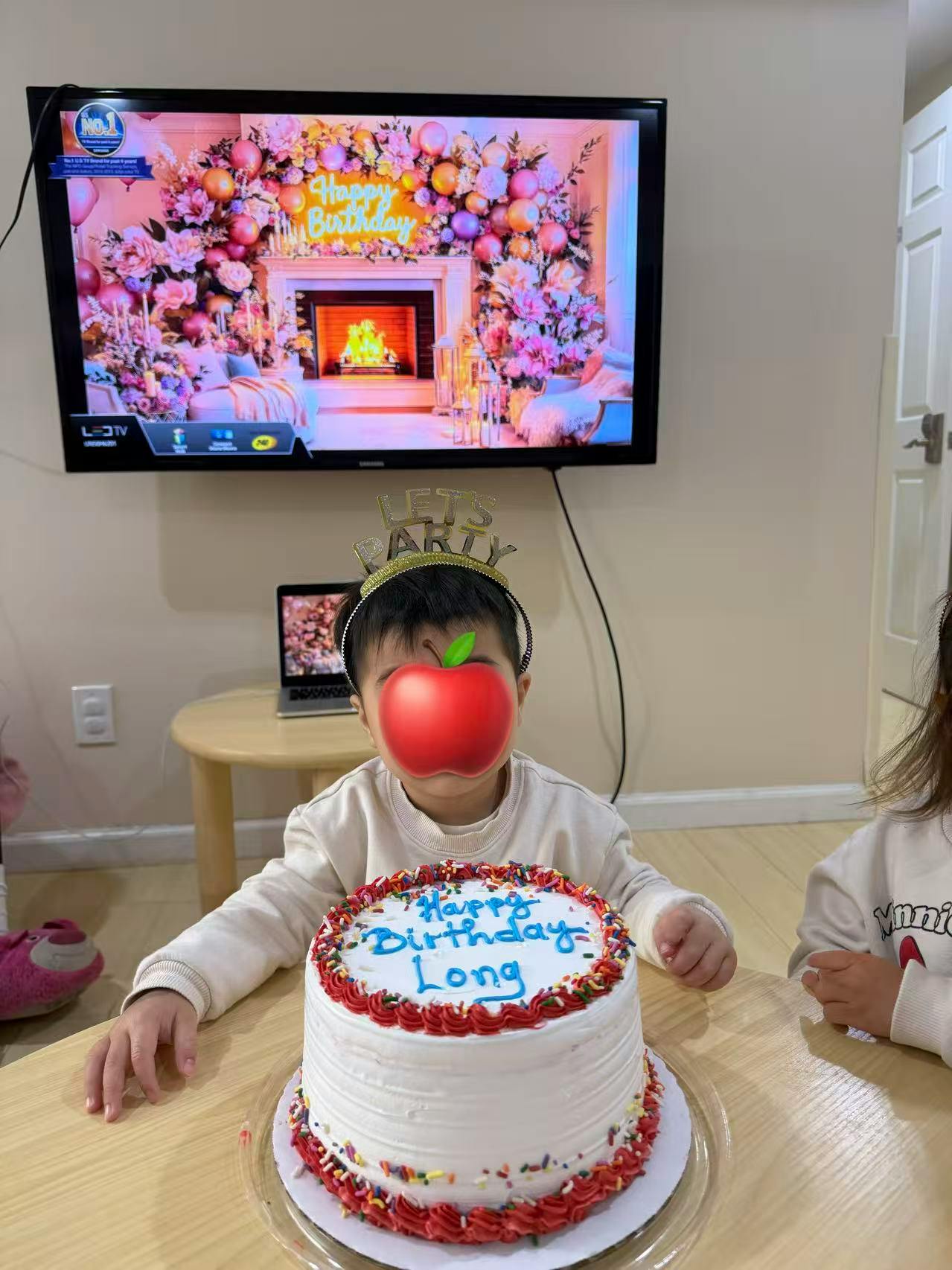 Child wearing a \"Lets Party\" headband, with a \"Happy Birthday Long\" cake