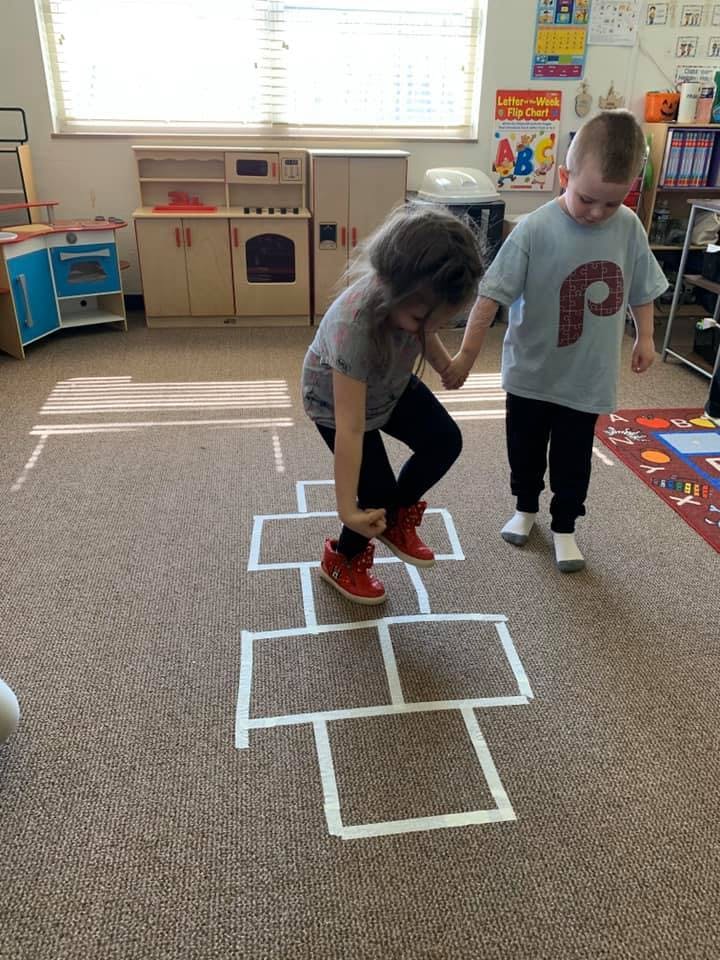 Two children playing hopscotch in a classroom