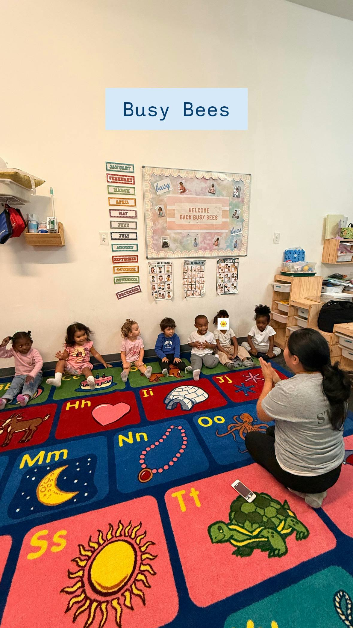 Adult and children sitting on a colorful alphabet rug in a classroom