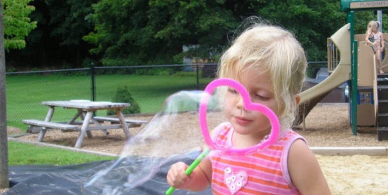 Child blowing bubbles with a heart-shaped wand on a playground