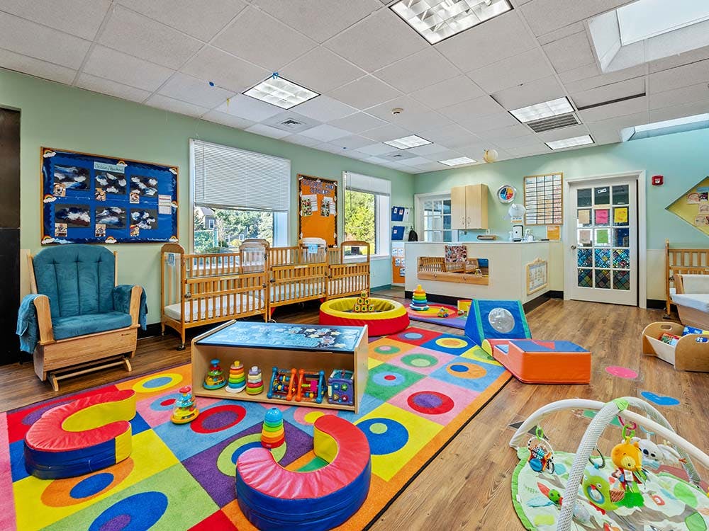 Colorful playroom with cribs, a rocking chair, and play mats