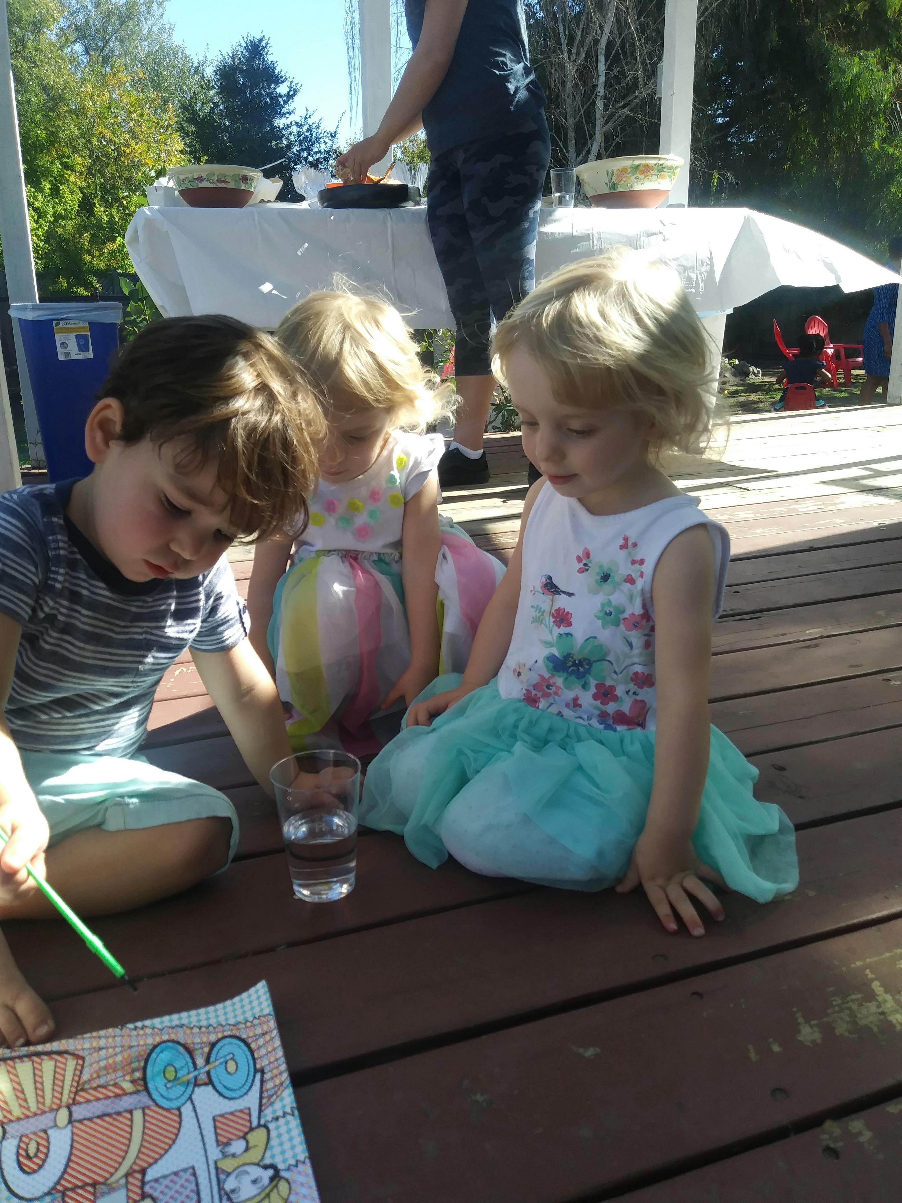 Three children sitting on a deck, one coloring