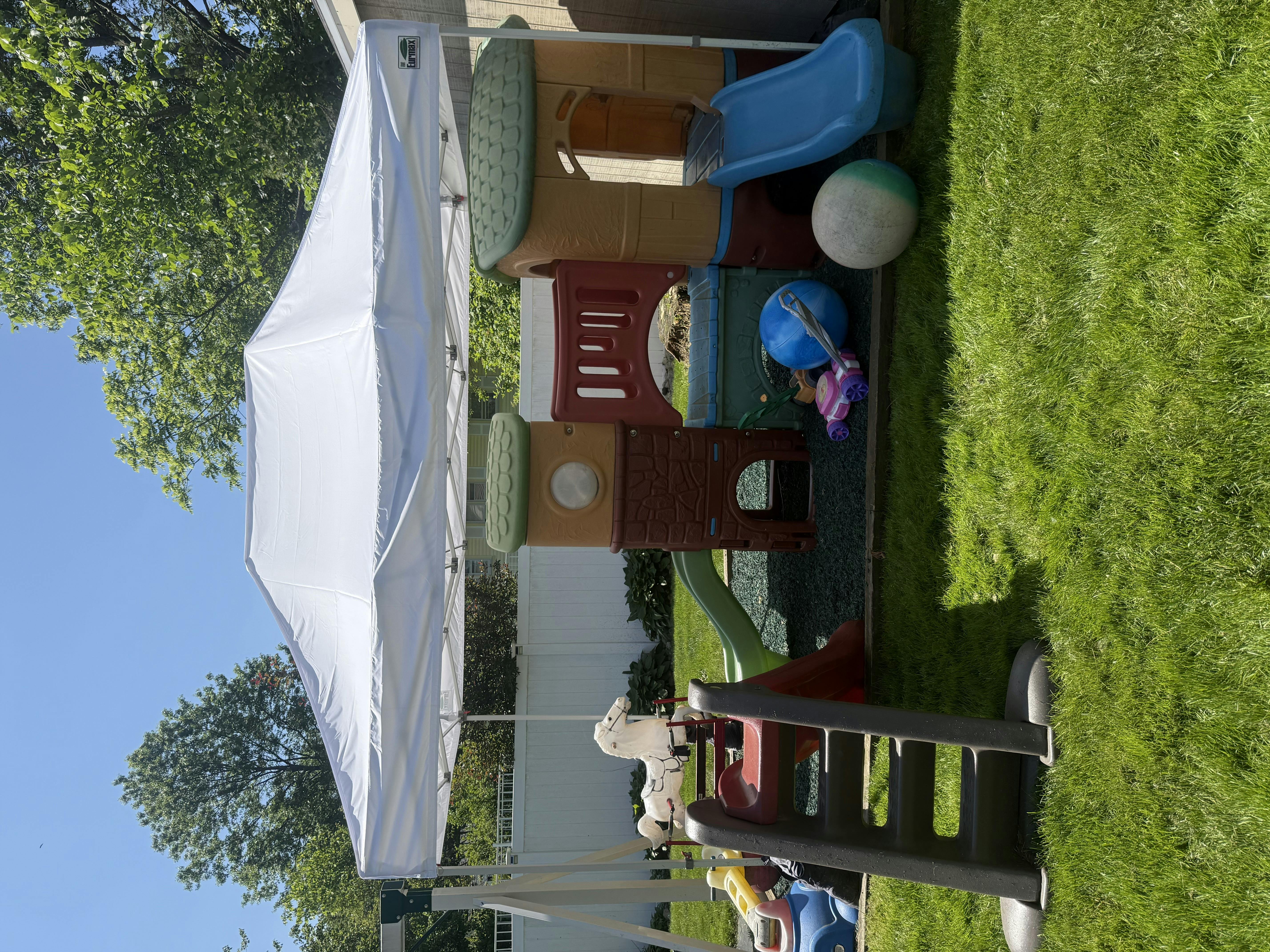 White canopy tent next to a colorful playground structure on grass