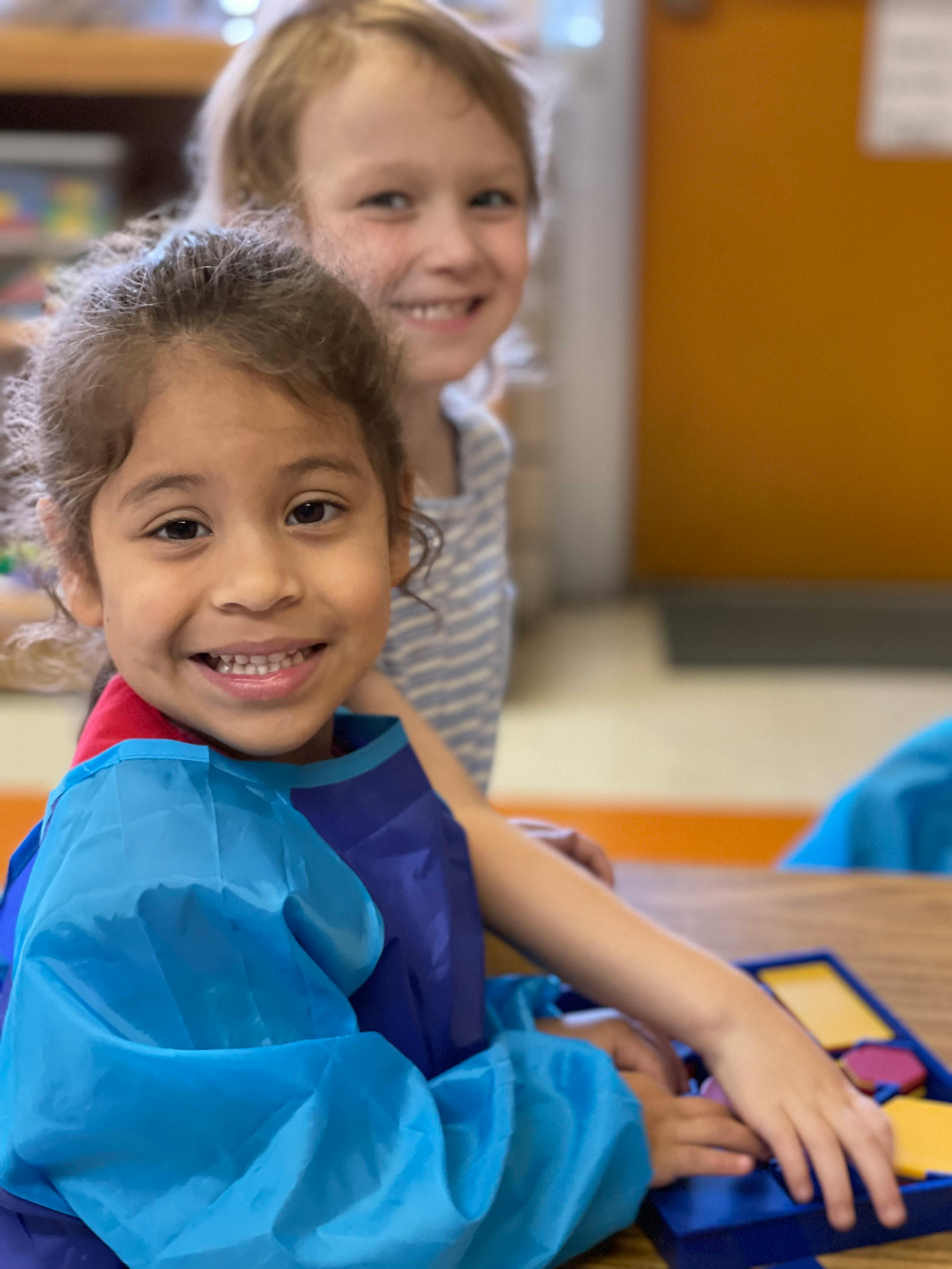Two children smiling, one in a blue art smock