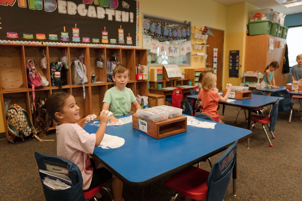Children playing with white foam on blue tables in a kindergarten classroom