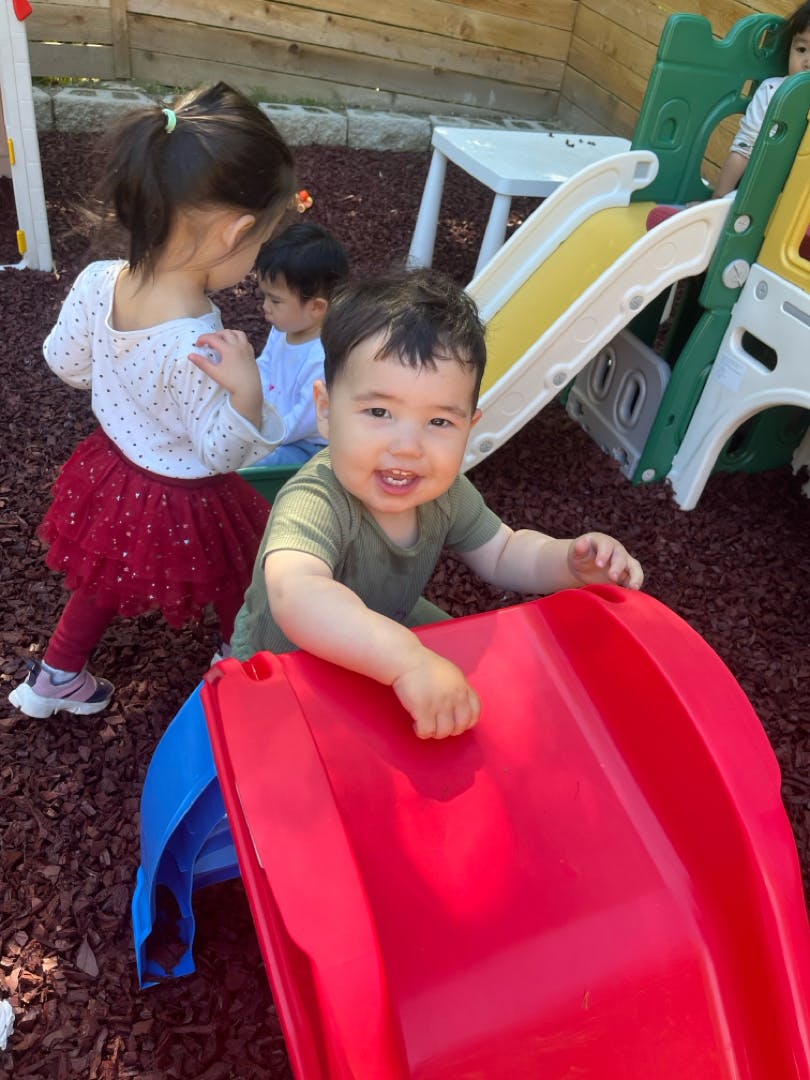 Smiling child on a red slide, with other children in the background